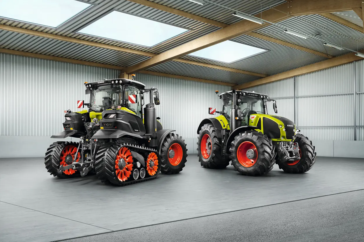  Deux tracteurs haute performance, l'un avec des chenilles orange, expos&eacute;s dans un entrep&ocirc;t spacieux